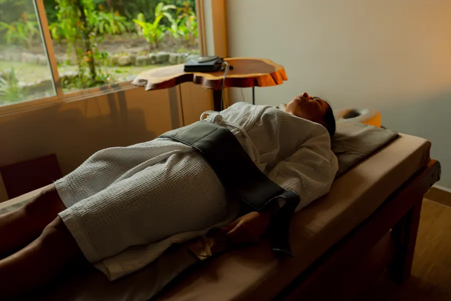 A guest resting under a blanket during a Bemer session beside a window onto the forest